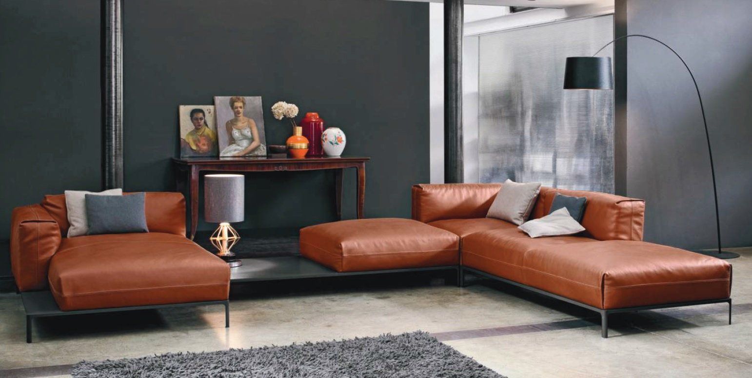 Soggiorno moderno con divano componibile in pelle marrone, parete grigio scuro e lampada da terra nera.