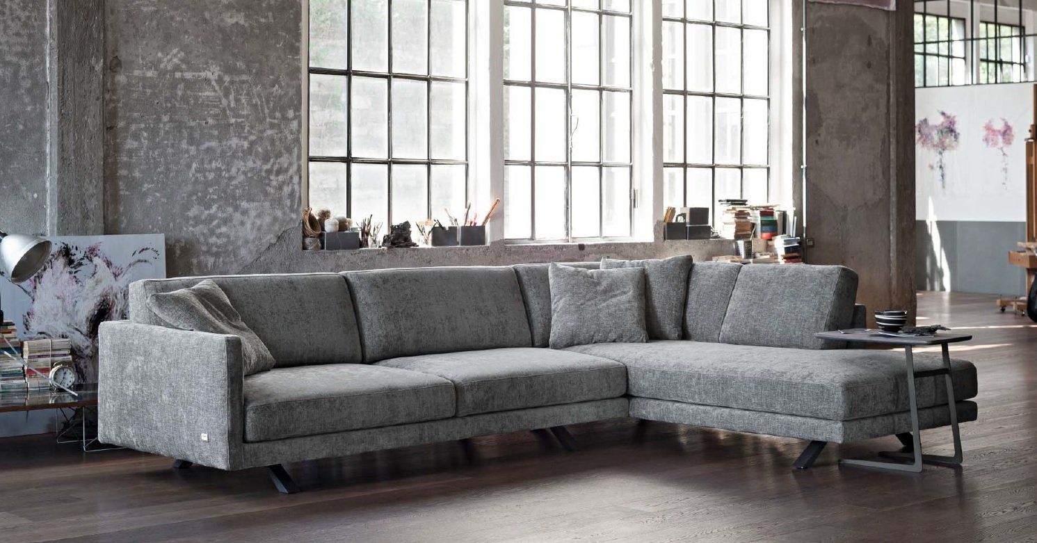 Divano componibile grigio in una stanza in stile loft con ampie finestre e architettura industriale.