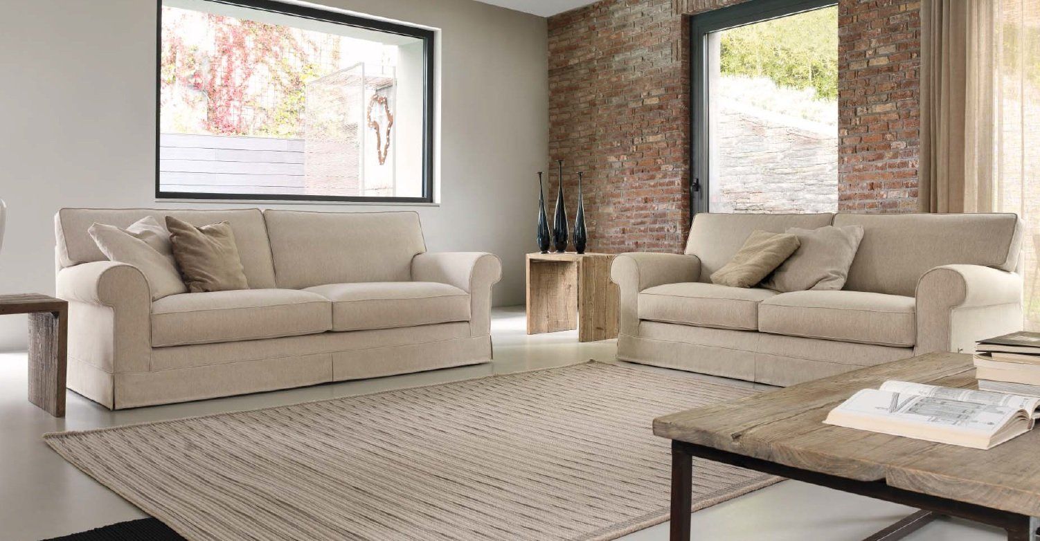 Soggiorno con due divani beige, un tappeto, un tavolino da caffè e una parete in mattoni.