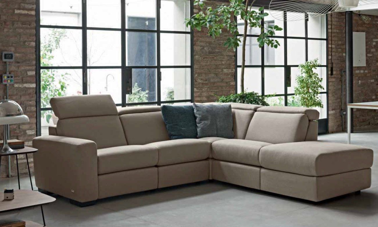 Divano componibile beige in una stanza moderna con ampie finestre e mattoni a vista.