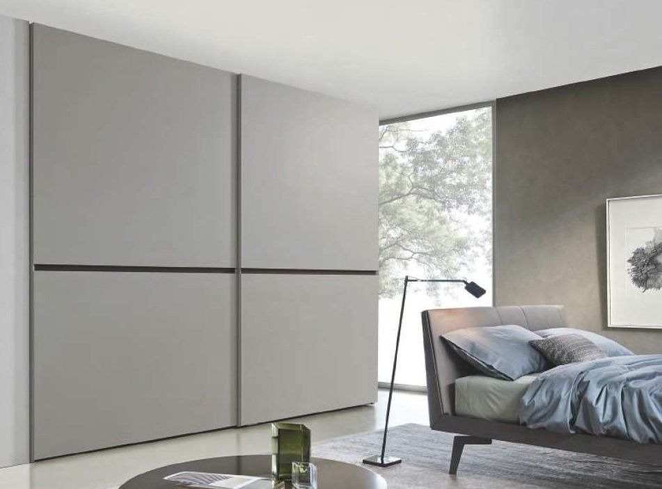 Camera da letto grigia con grande armadio, letto, tavolo rotondo e una finestra con un albero.