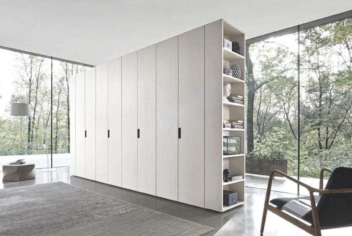 Moderno armadio bianco con ripiani aperti e ante in una stanza con ampie finestre.
