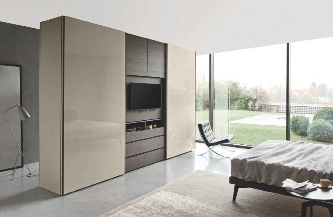Camera da letto moderna con armadio beige lucido, sezione centrale in legno scuro con TV, ampia finestra e mobili minimalisti.