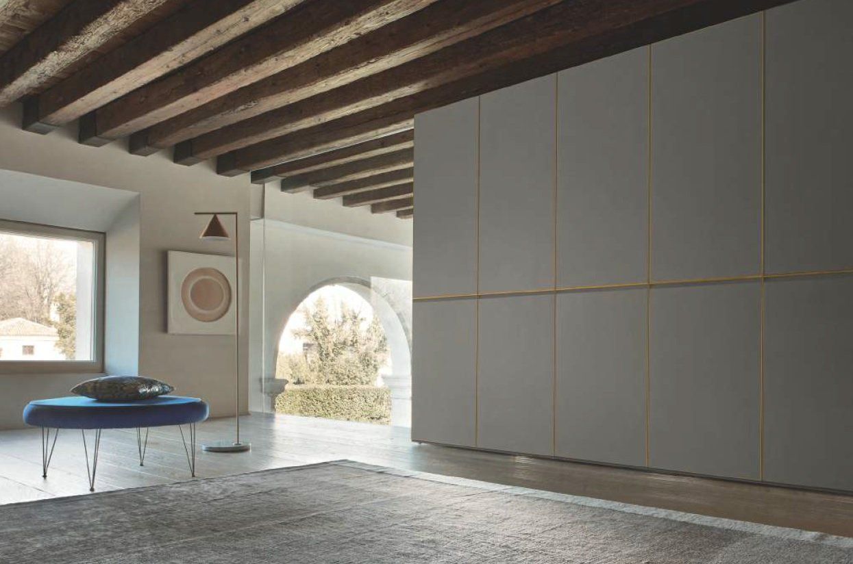 Grande armadio grigio con finiture dorate in una stanza con travi in legno a vista, arco e pouf blu.