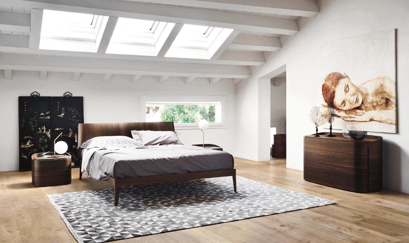 Camera da letto con pavimento in legno, letto, cassettiera, opere d'arte e lucernari in un ambiente luminoso e moderno.