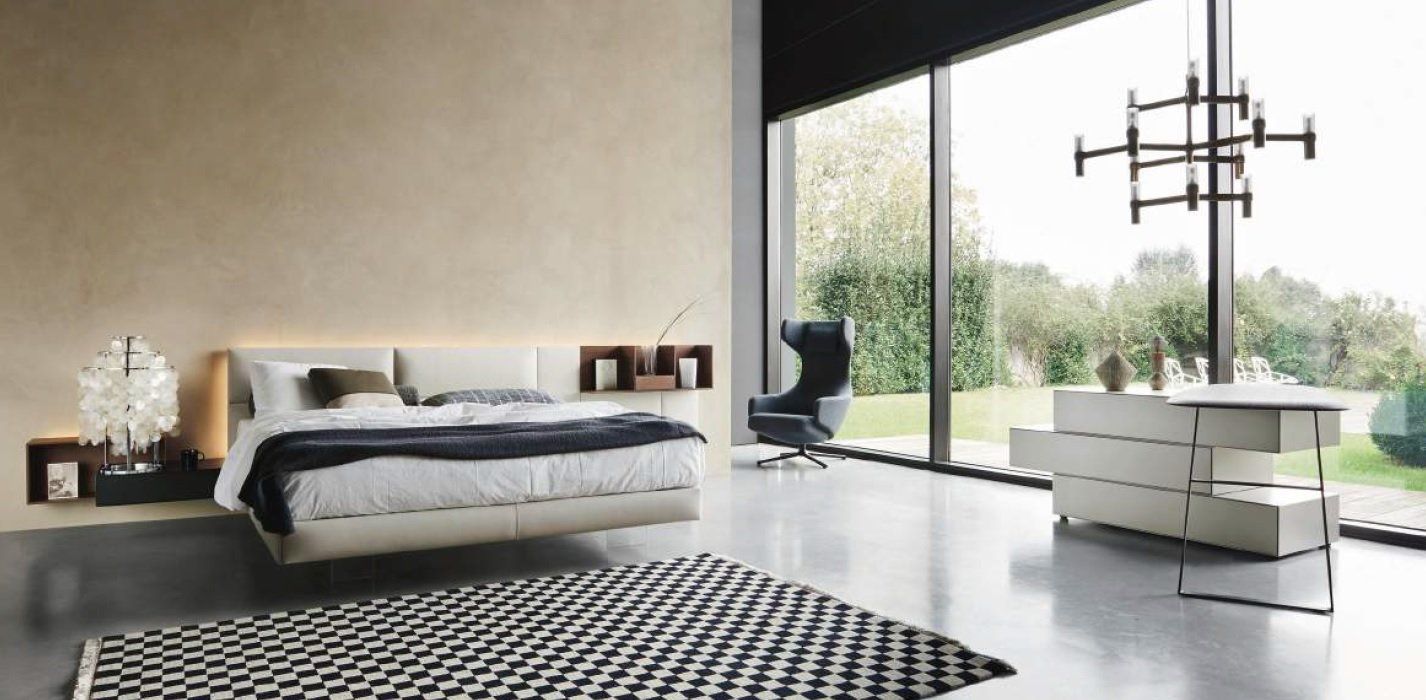 Camera da letto moderna con ampia finestra, letto e tappeto a fantasia.