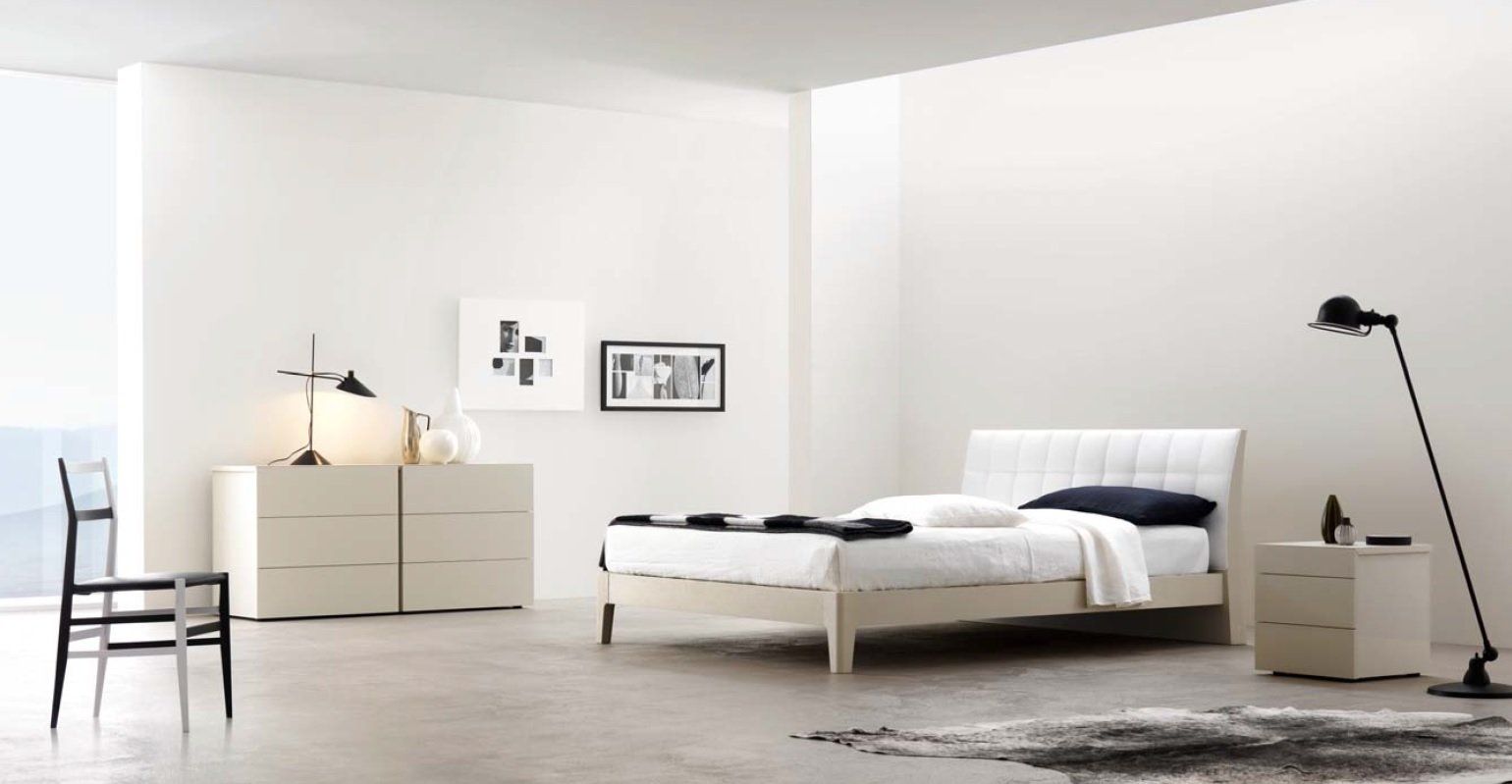 Moderna camera da letto bianca con letto, cassettiera, comodino, sedia nera, quadri e lampada da terra.