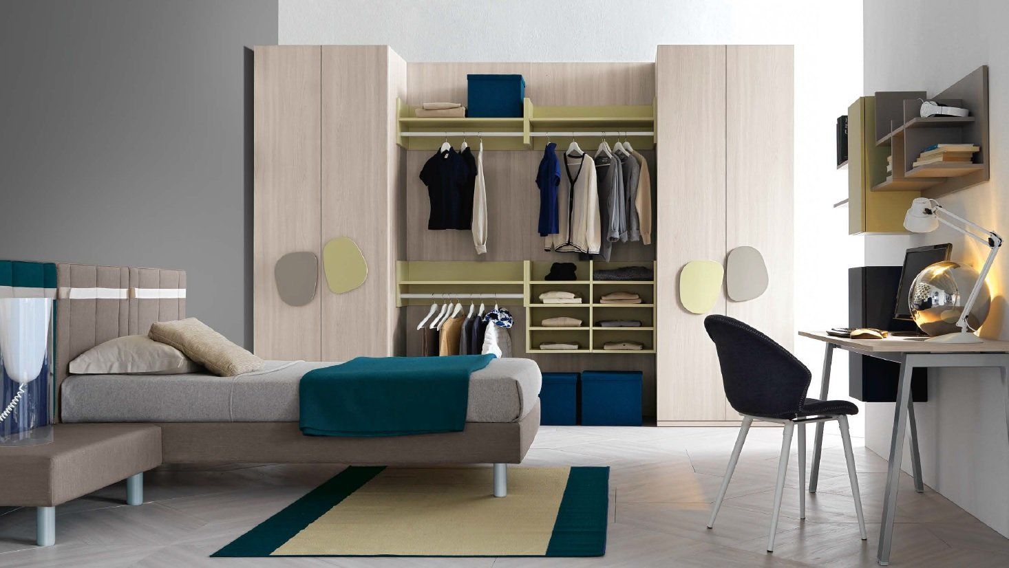 Camera da letto con armadi e letto in legno chiaro. Scrivania con sedia nera e dettagli colorati.