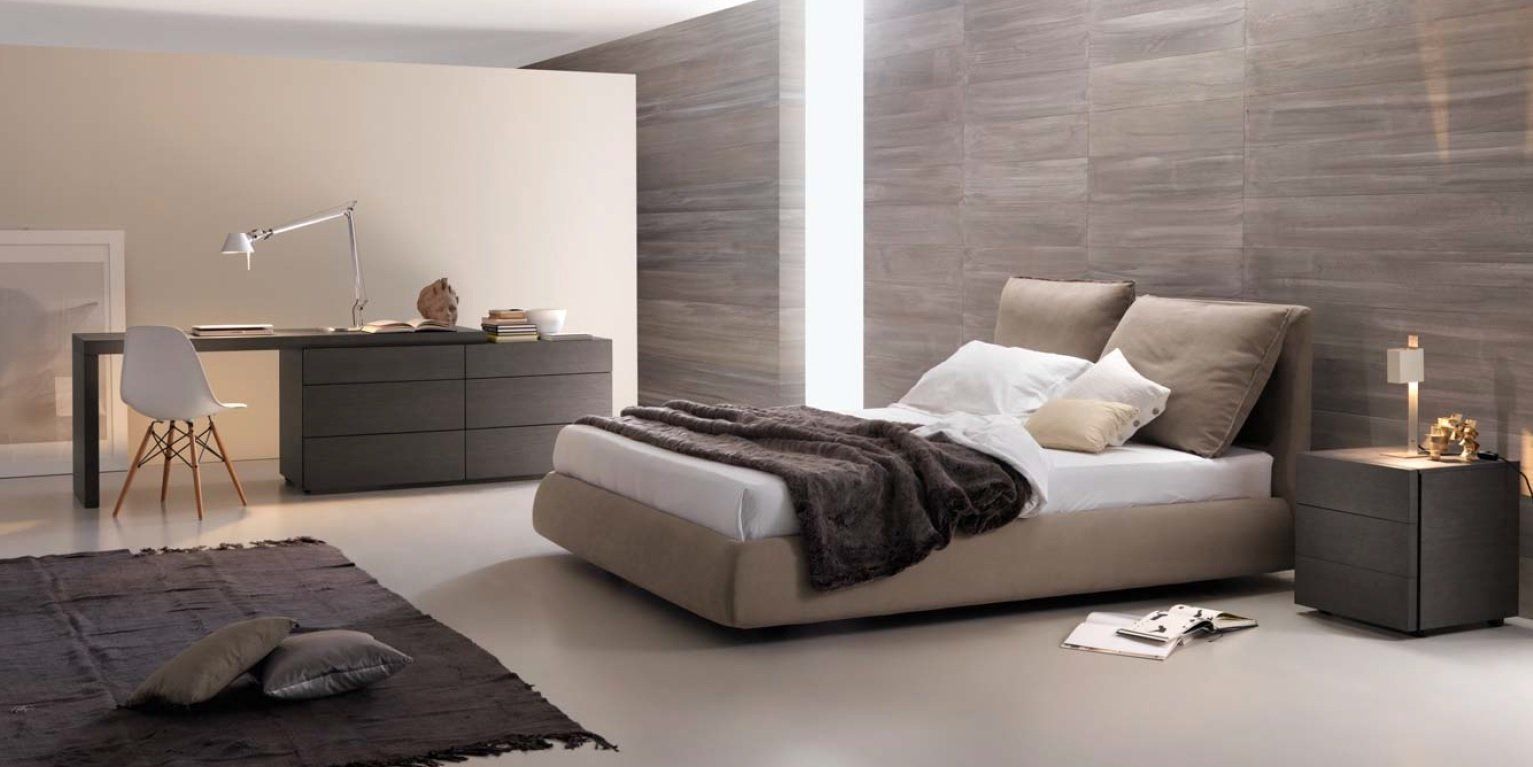 Camera da letto moderna con letto, scrivania e tappeto. Palette di colori neutri, parete in pietra e illuminazione calda.