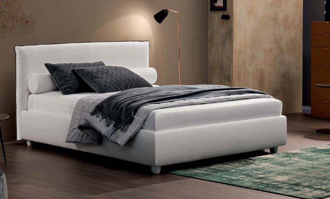 Letto imbottito bianco con cuscini e coperta, in una camera da letto dai toni neutri con un tappeto verde.