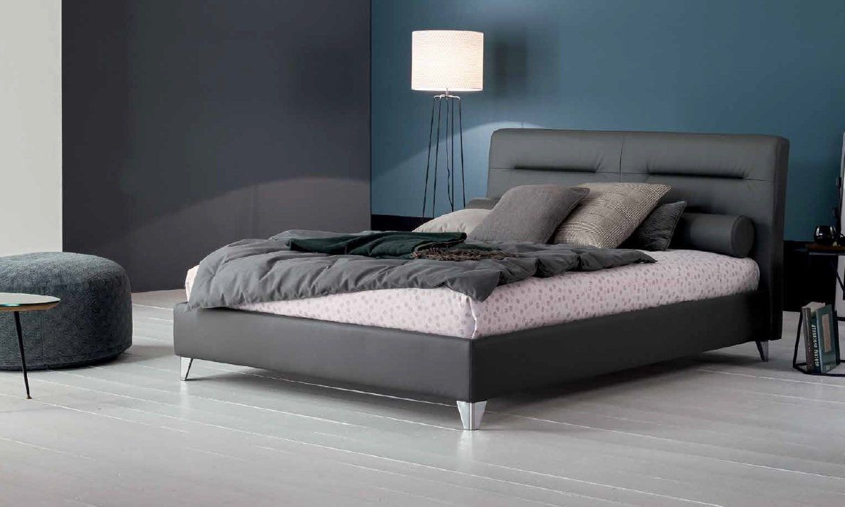 Letto grigio con cuscini, coperta e testiera, in una camera da letto moderna.
