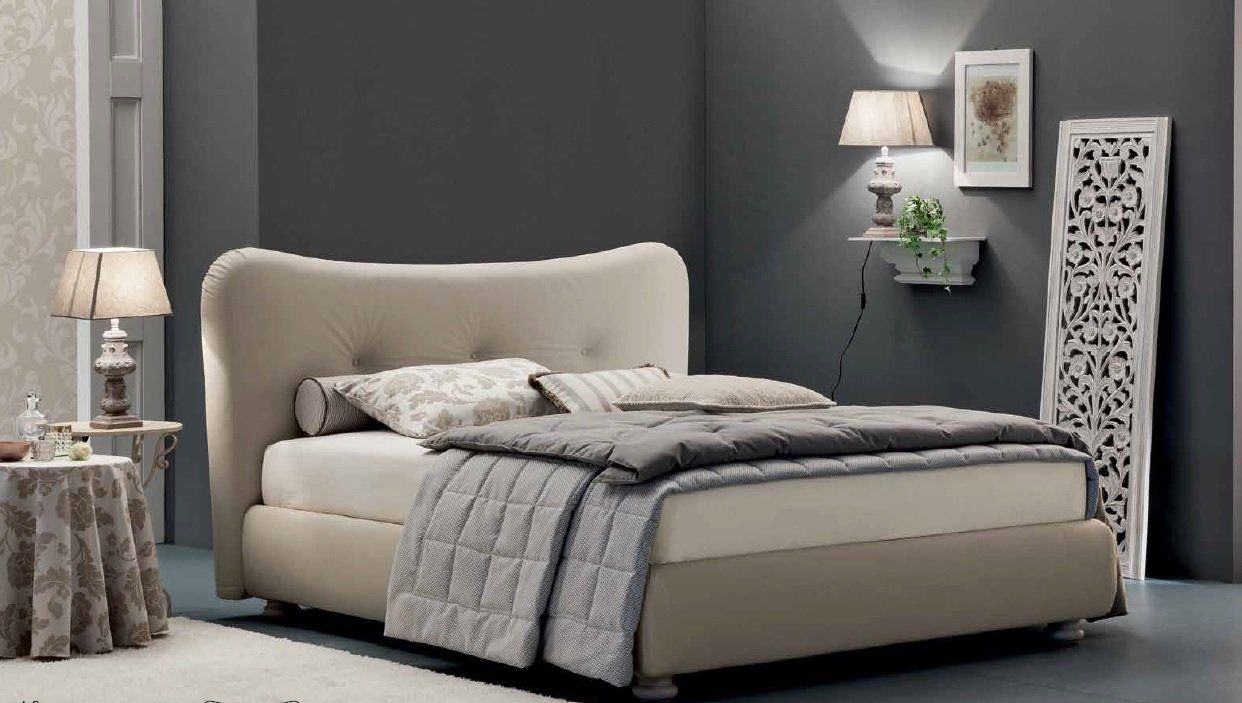 Letto imbottito beige con coperta a fantasia, comodini e parete grigia.