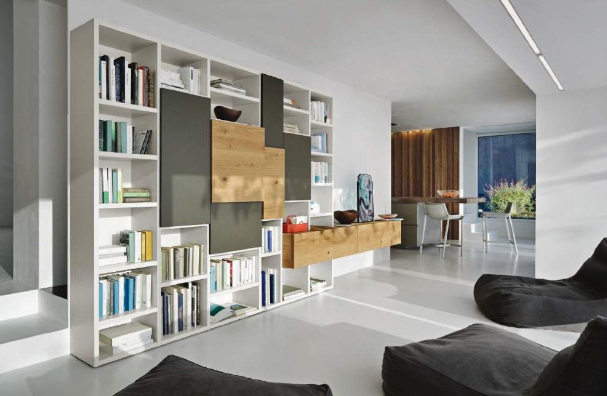 Moderna libreria bianca con inserti in legno integrati, piena di libri, in un luminoso soggiorno.