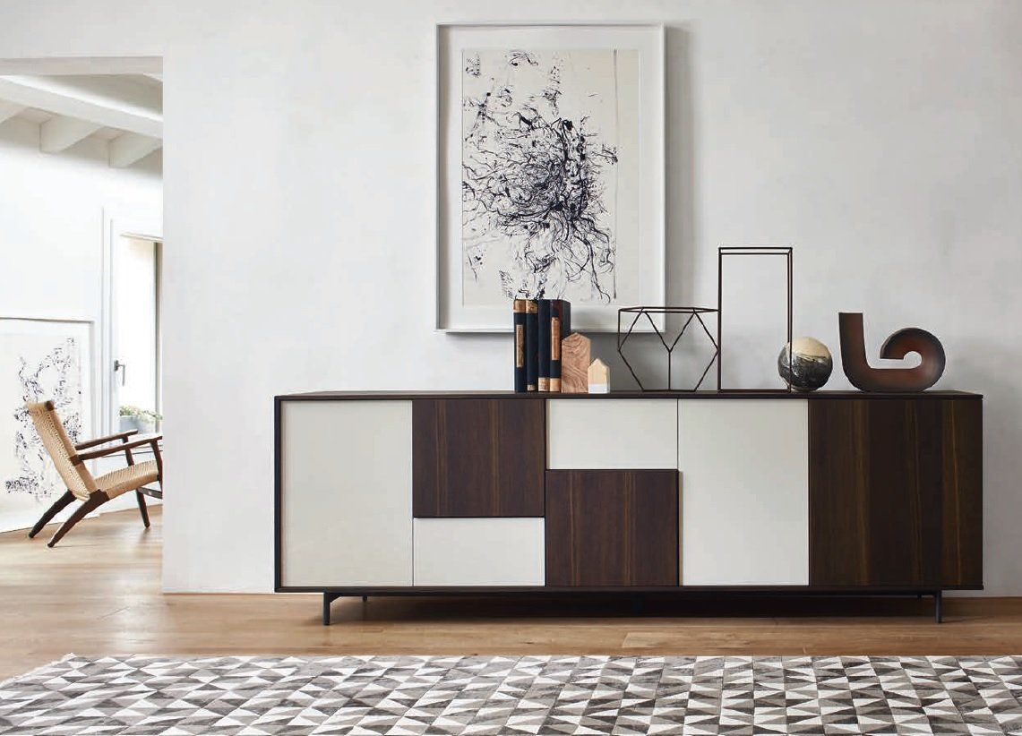 Credenza moderna con pannelli in legno scuro e bianchi, decorata con decorazioni, contro una parete bianca con opere d'arte.