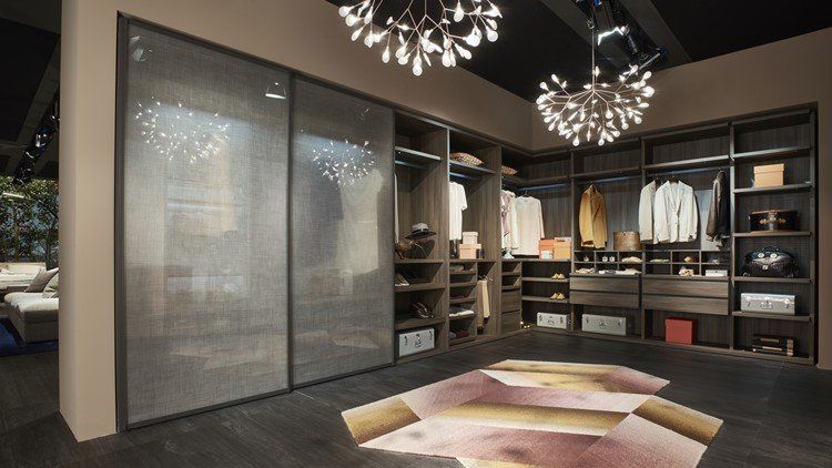 Cabina armadio con porte scorrevoli in vetro, appendiabiti e pavimento decorato. Legno scuro e toni neutri.