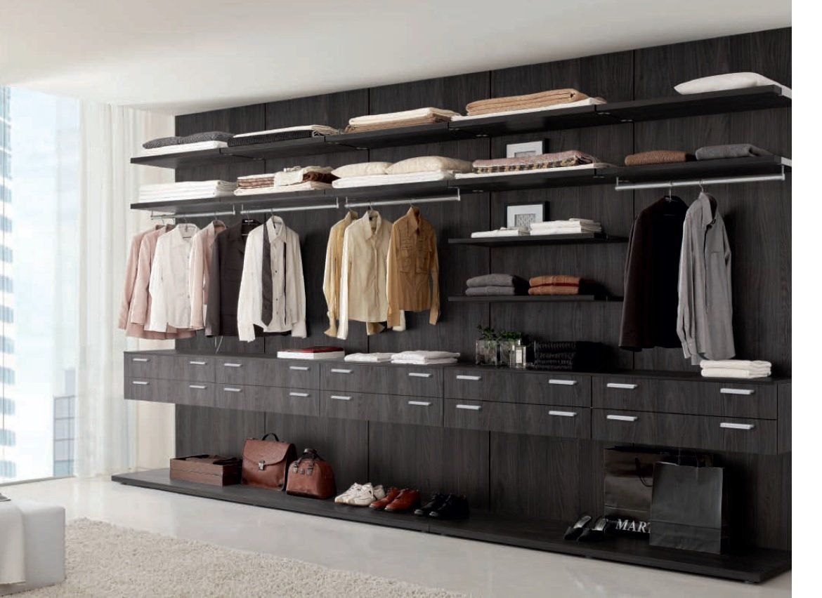 Moderna cabina armadio con ripiani, cassetti e aste appendiabiti in legno scuro. I vestiti sono ben organizzati.