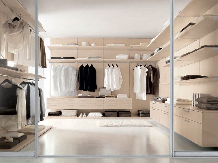 Cabina armadio con ripiani in legno chiaro, appendiabiti, cassetti e un piccolo tappeto.