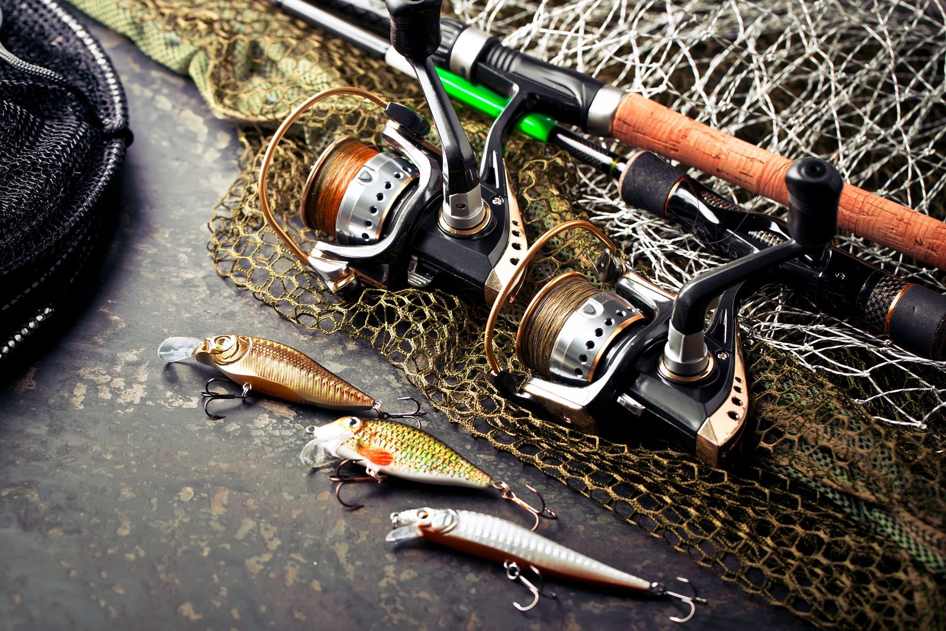 Fishing reels, rods, lures, and a net on a surface.