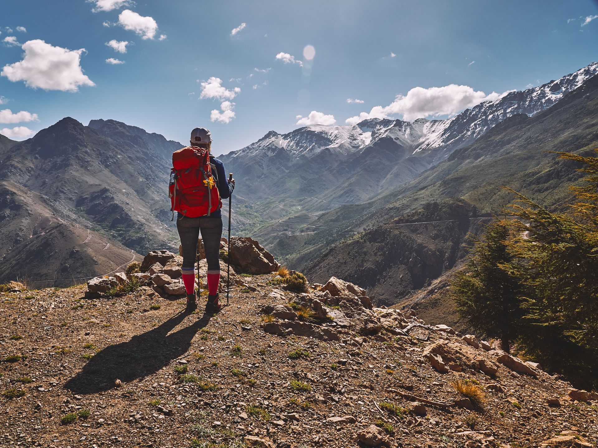 A man with a backpack and hiking poles is standing on top of a mountain.