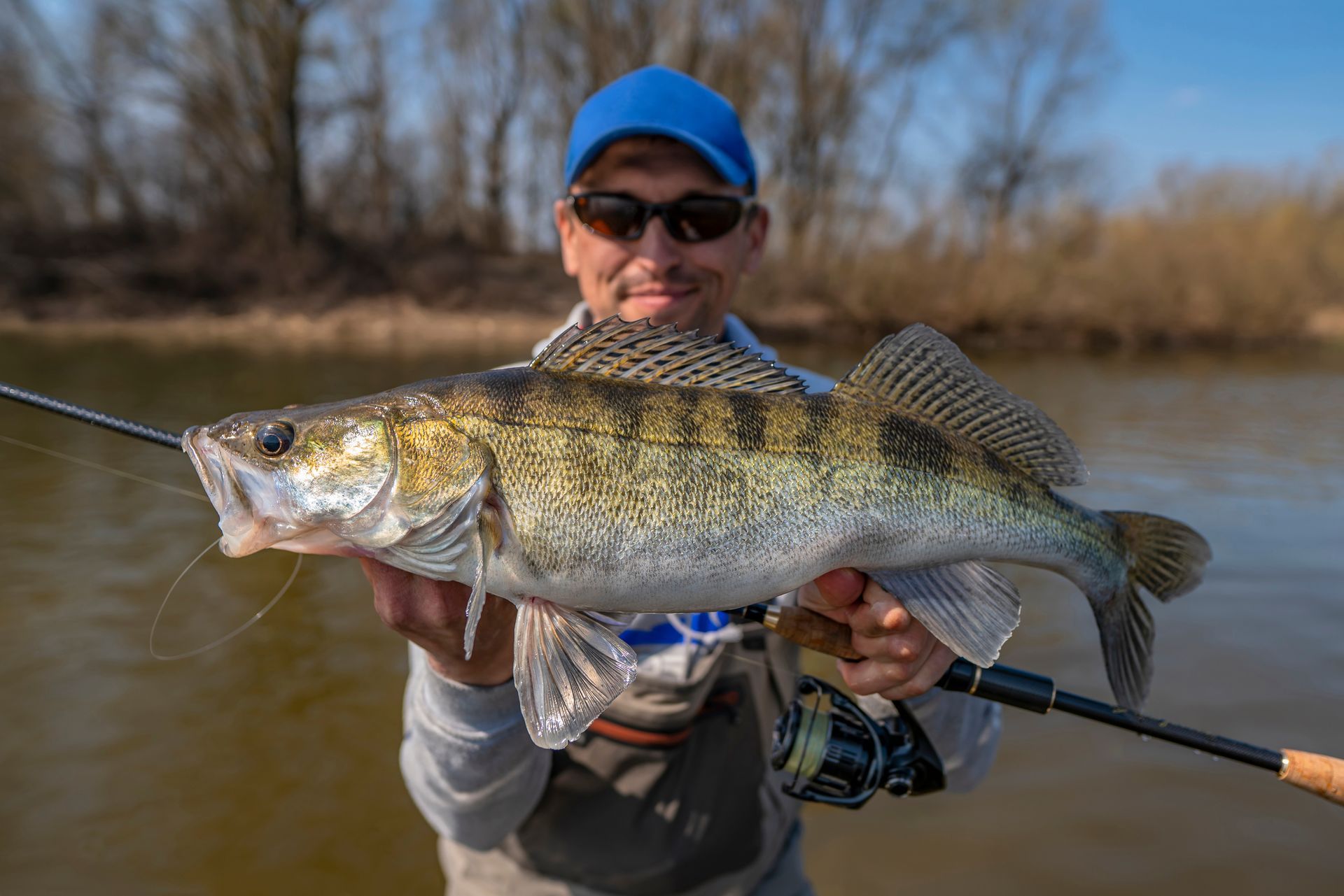 A man is holding a large fish in his hands next to a river.