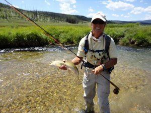 A man is fishing in a river and holding a fish.