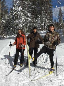 Three people are standing in the snow with skis and poles.