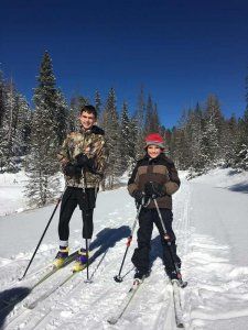 Two young boys are cross country skiing in the snow.