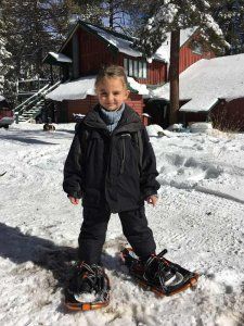 A young boy is standing in the snow wearing snowshoes.