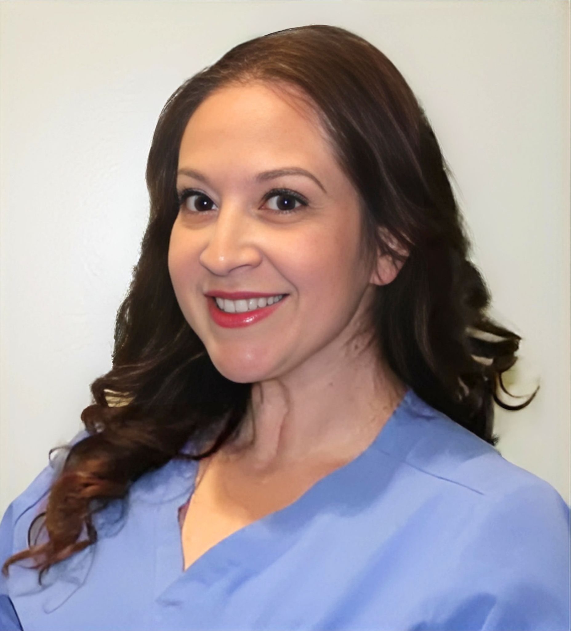 A woman in a blue scrub top is smiling for the camera.