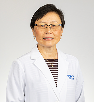 A woman wearing glasses and a white lab coat is standing in front of a white background.