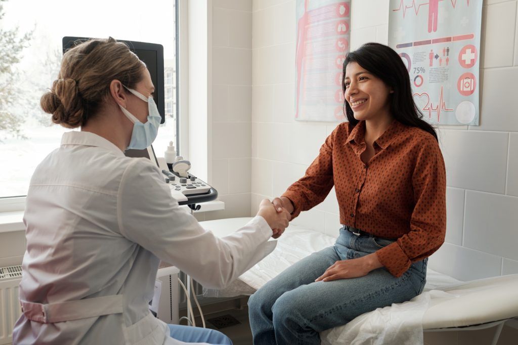 A woman is sitting on a bed shaking hands with a doctor.