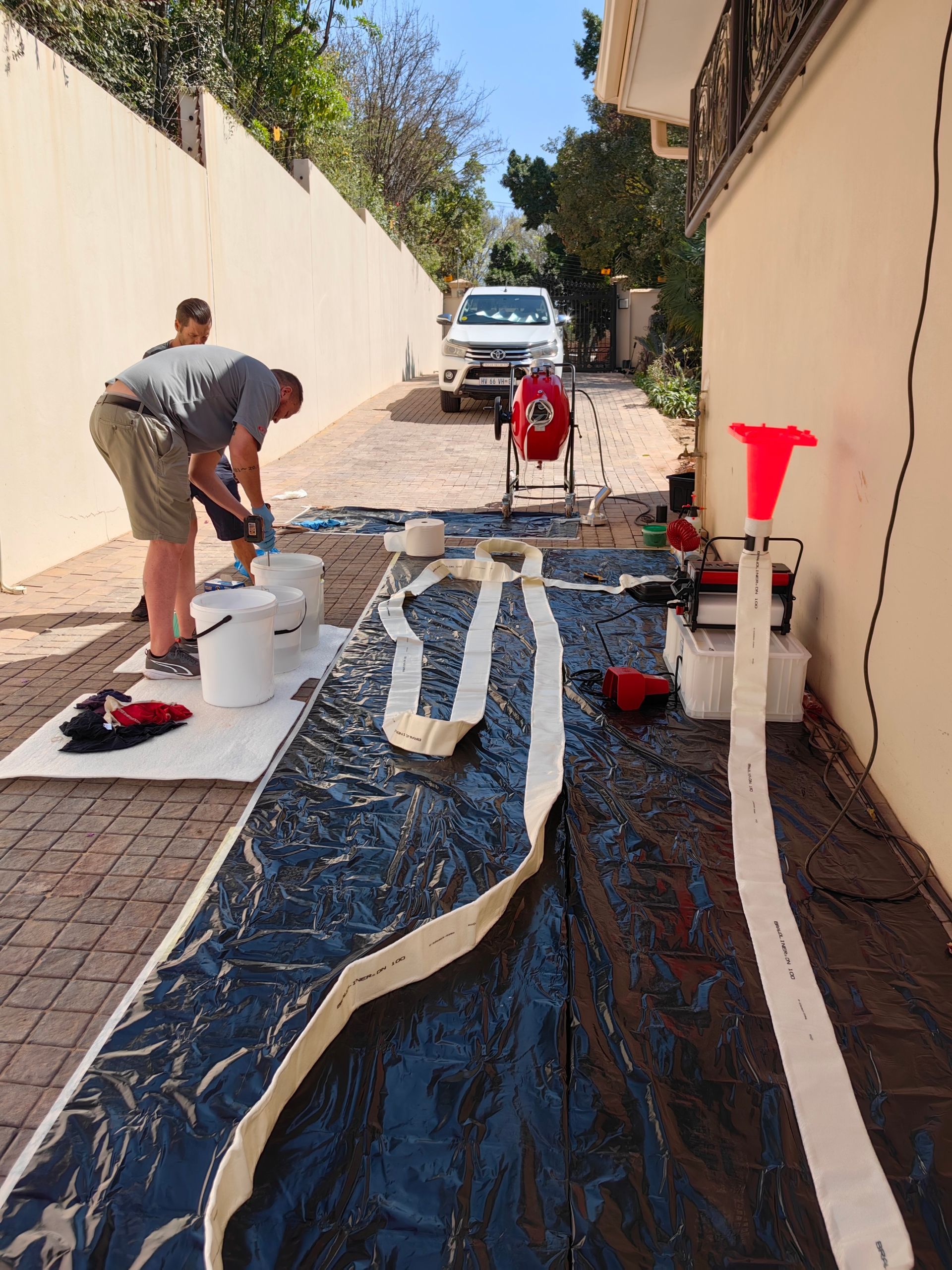 Two men are working on a hose outside of a building.