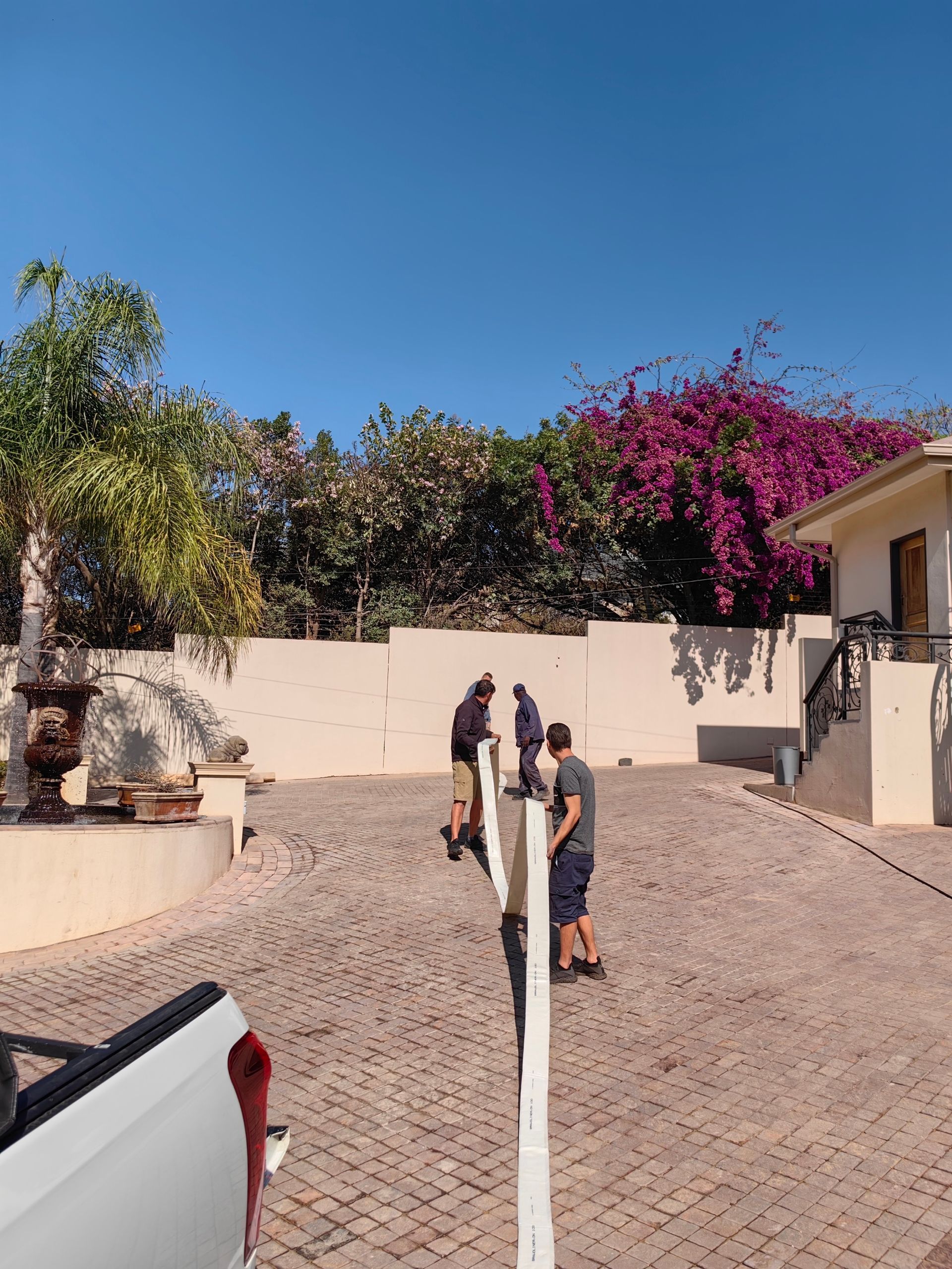 A group of people are standing in front of a house with purple flowers.