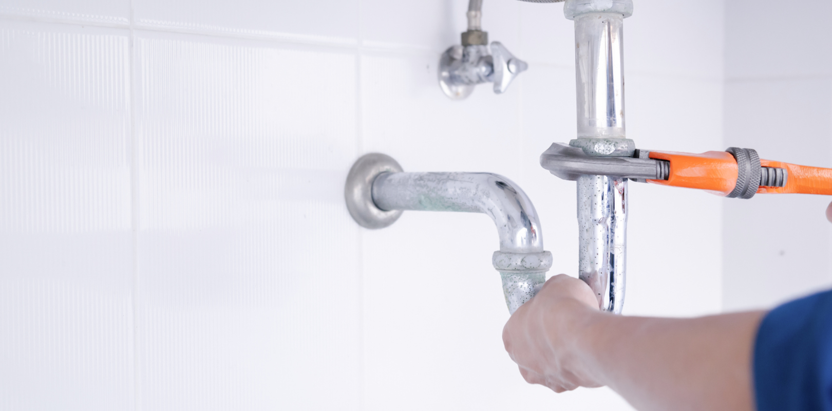 A plumber is fixing a sink pipe with a wrench.