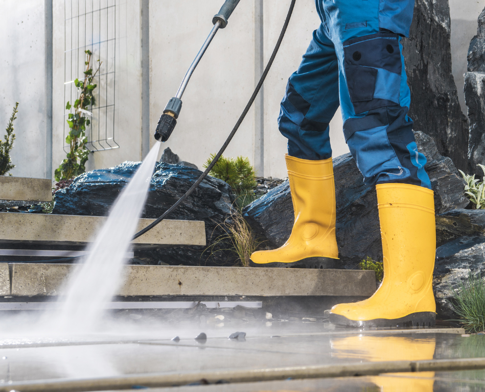 A person wearing yellow boots is using a high pressure washer to clean stairs.