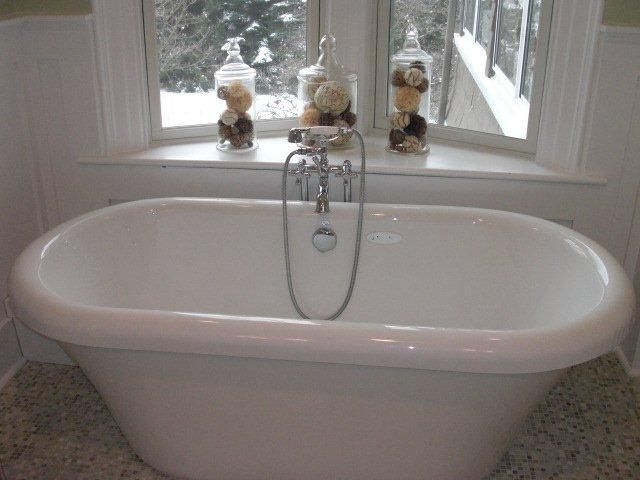 A white bathtub in a bathroom next to a window