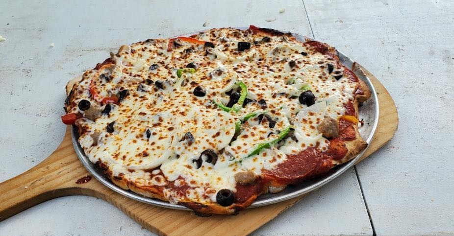 A pizza is sitting on a wooden peel on a table.