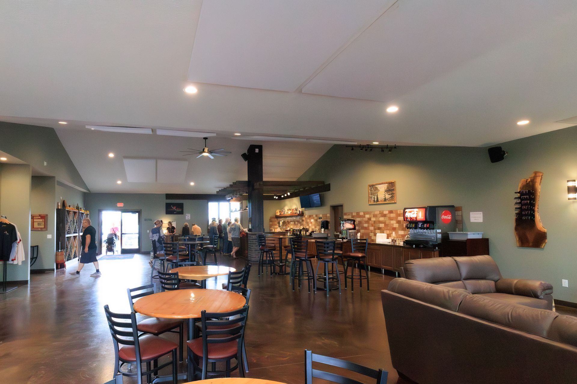 Interior of a restaurant or bar with tables, chairs, bar area, and people. Green walls, wood and brown decor.