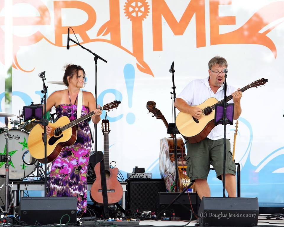 Two people on stage playing acoustic guitars at an outdoor music festival.