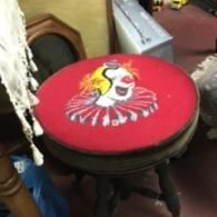 A red circular stool top featuring an illustration of a clown, set in a cluttered indoor space.