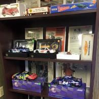 A wooden shelf displaying a collection of miniature NASCAR race car models in their original boxes.