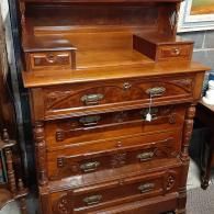 A tall, ornate wooden dresser with a small hutch, four large drawers, two small top drawers, and metal handles.