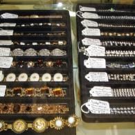 Two jewelry display trays hold various bracelets, most featuring price tags, inside a glass showcase.