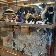 A glass display cabinet filled with crystal glassware on the bottom shelf and various decorative items on the top shelf.