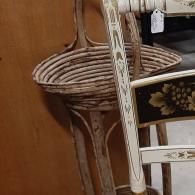A decorative light-colored wooden chair back with floral motifs in the foreground, and a wicker basket stand behind.