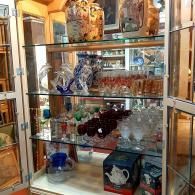 A glass display cabinet filled with decorative items, including ceramic vases, glassware, and boxed tea accessories.