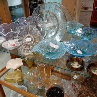 Glass bowls, plates, and dishes of various colors and designs are displayed on multiple shelves in a retail shop.
