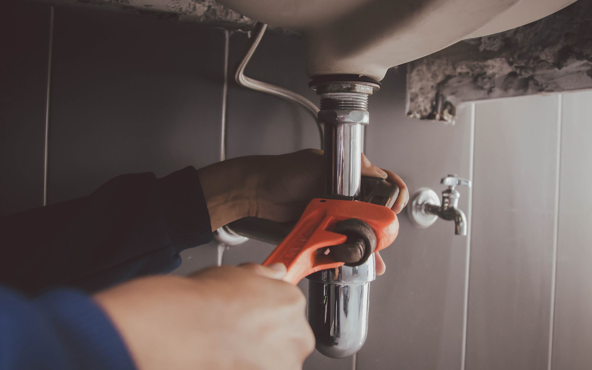 A person using a wrench to work on plumbing under a sink.