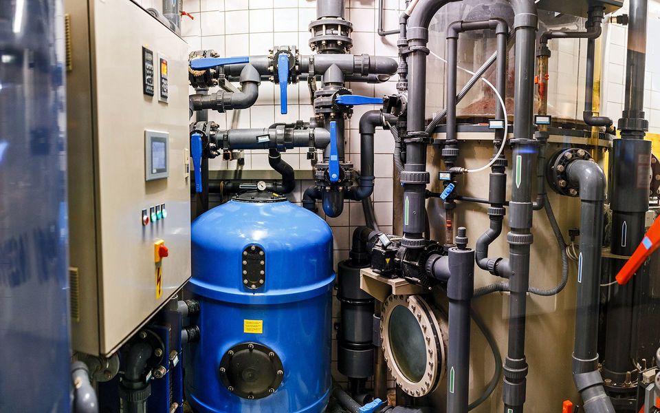 Blue and black pipes and tanks, with a control panel, in an industrial setting.