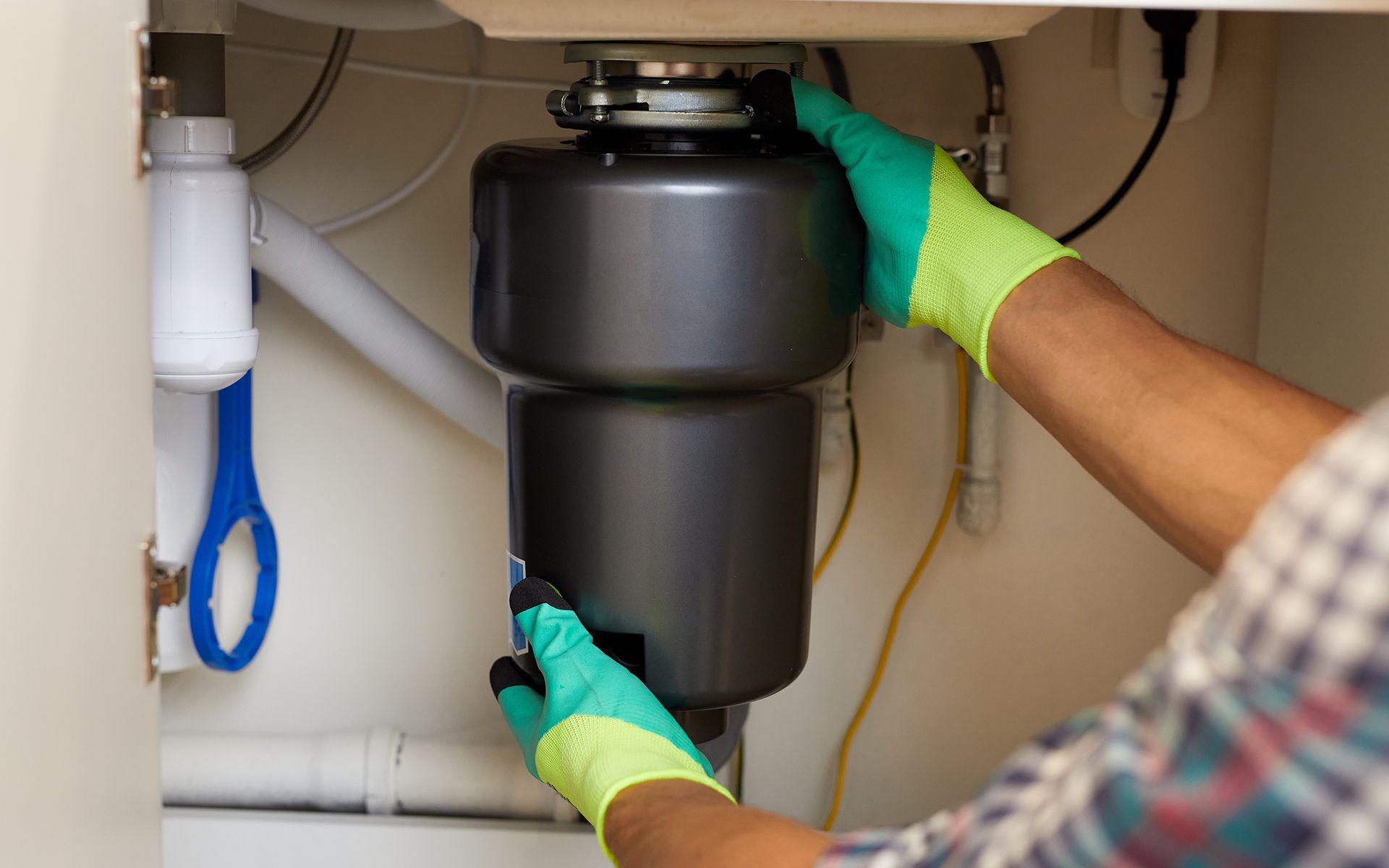 Person in green gloves installing a garbage disposal under a kitchen sink.